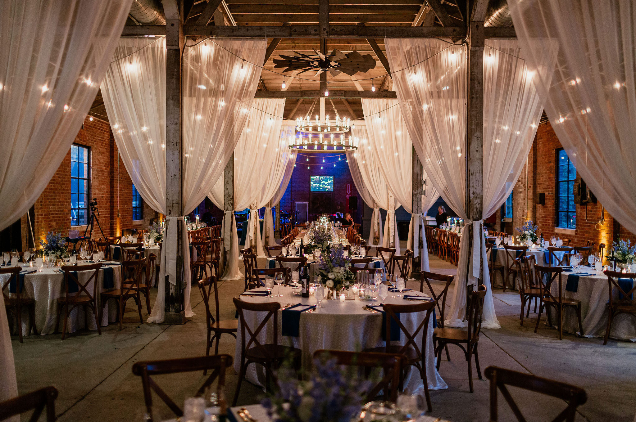 wedding reception with tables, white draping, a chandelier and market lights 