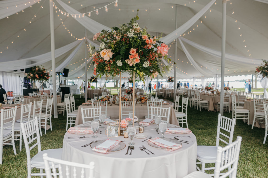 lake wedding reception tent with white tables and chairs and tall flower arrangements