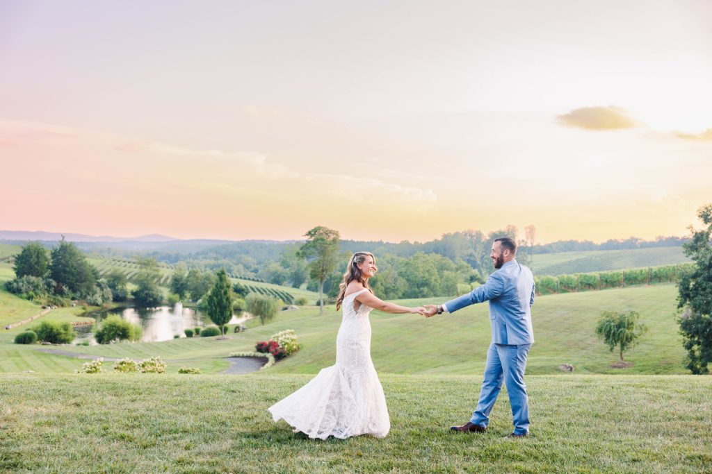 bride and groom hold hands at sunset outside stone tower winery with vineyards in the background 