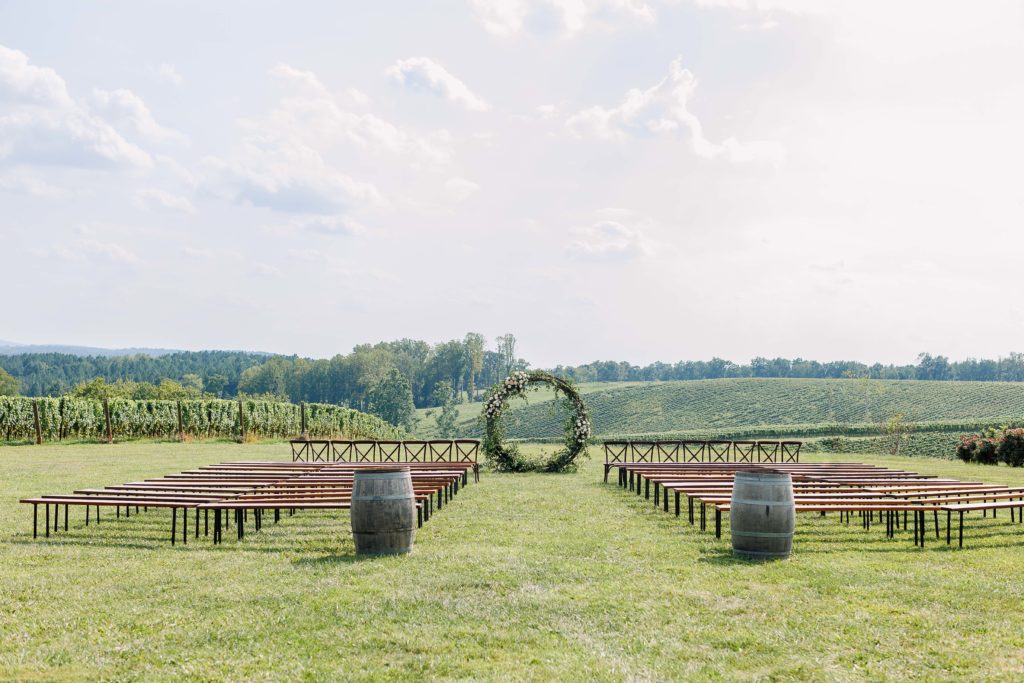 wedding ceremony set up in front of the vineyards with a circular arch and wood benches and seating