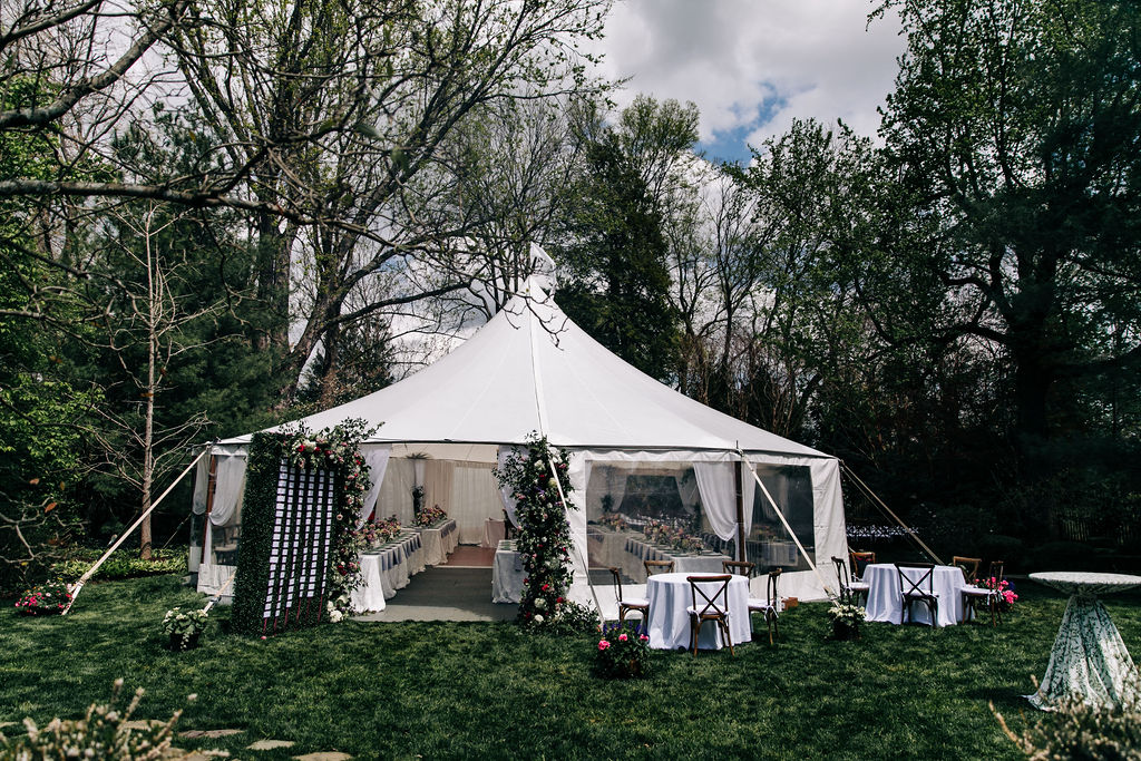 white backyard wedding reception tent with tables, chairs, a large seating charted flower arrangements 