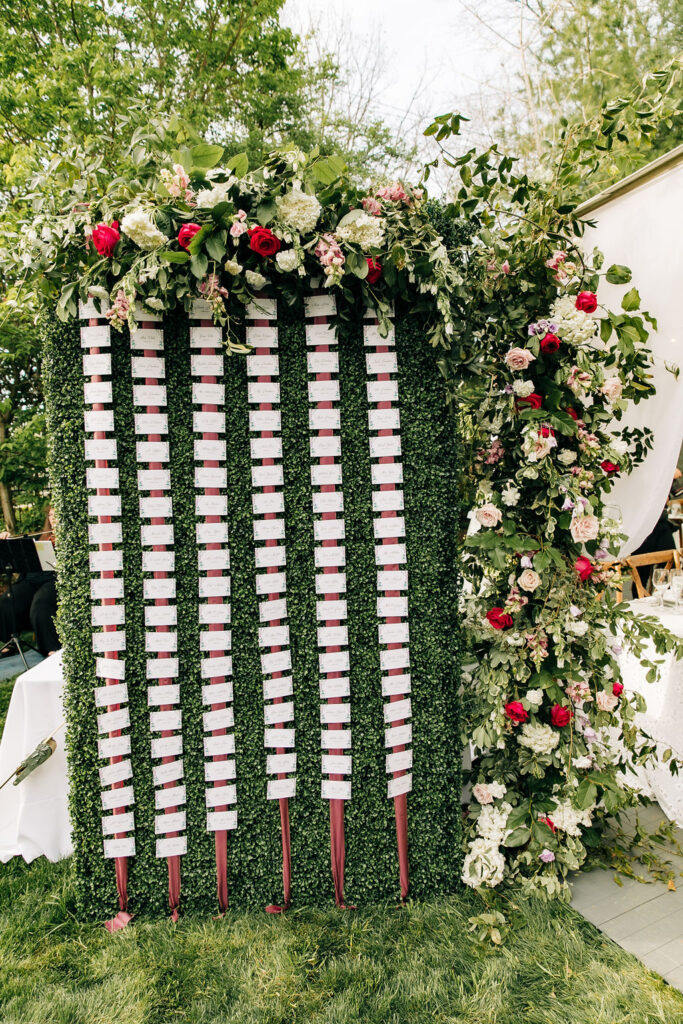 tall seating chart with green background and large red and white  flower arrangement 