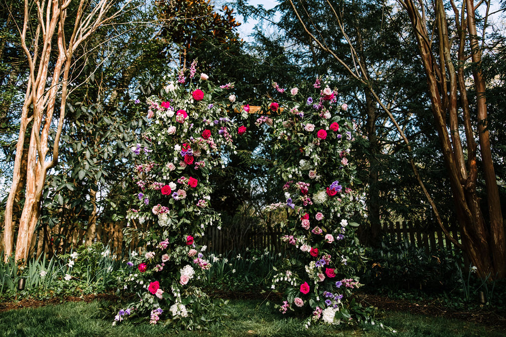 large floral wedding ceremony arch with red, white, pink and purple flowers 