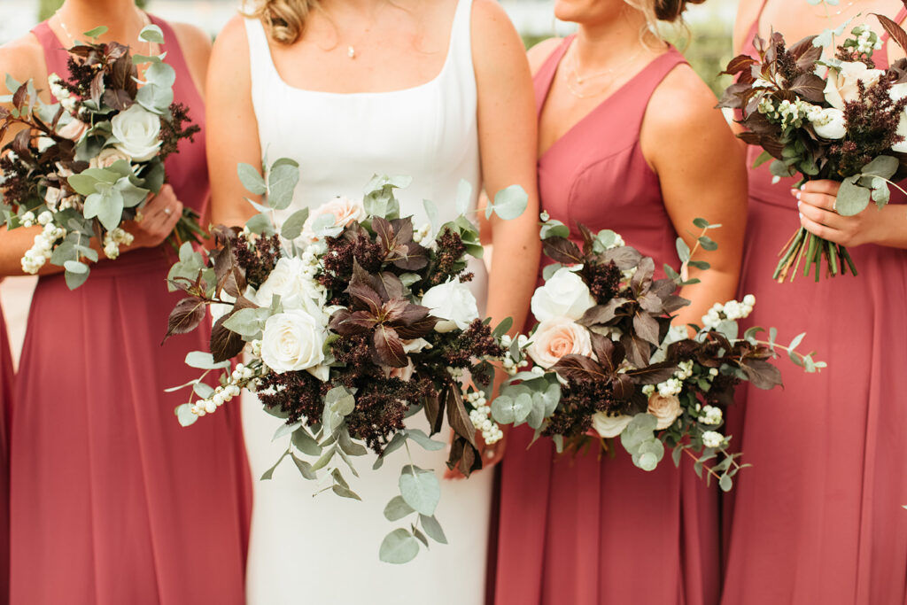 The bride and her bridal party wearing pink dresses with a close up shot of their green, white and maroon bouquets 