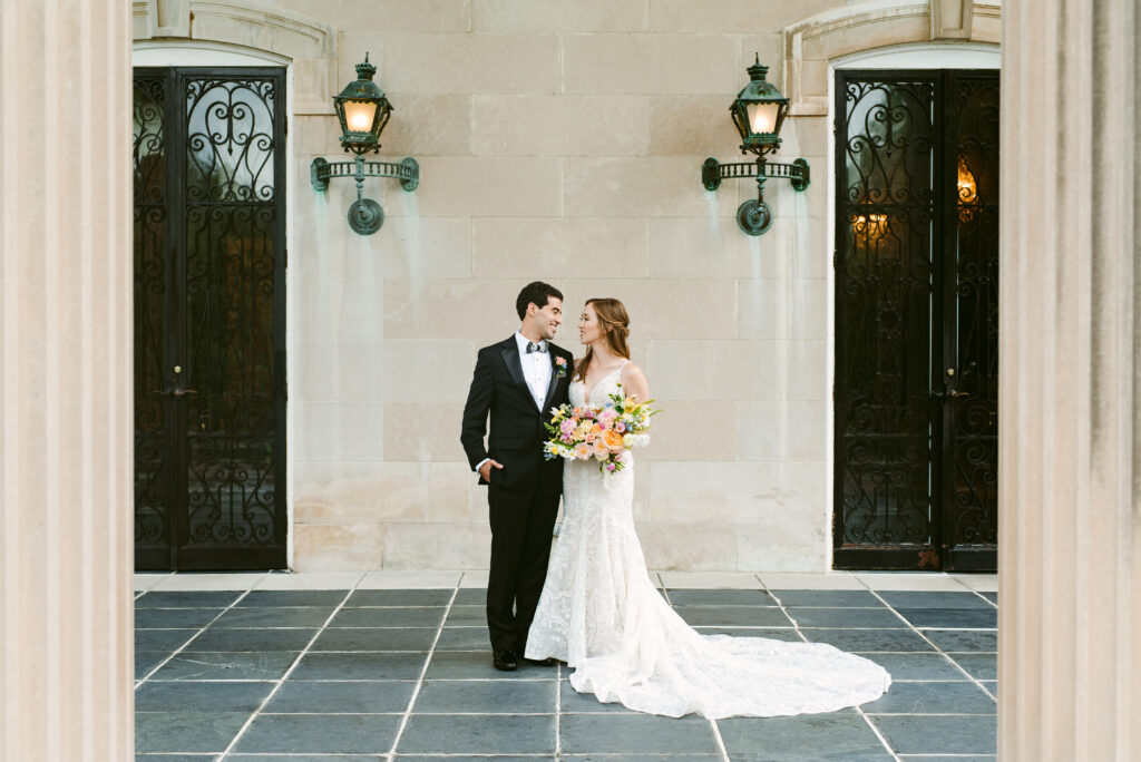 Bride and groom take a formal photo together on the patio of spindletop hall with glass iron doors and lanterns framing their image perfectly