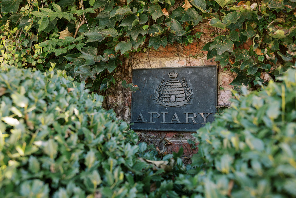 Apiary wedding venue garden sign with a beehive icon on an iron sign surrounded by green vines